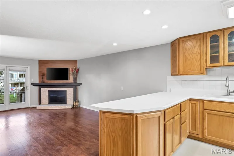 Open concept living area featuring wood-finish flooring, a corner fireplace with a mantel, and French doors leading to the lake, boardwalk and pool — 43 Breezy Knoll Lane, Lake St. Louis, MO 63367
