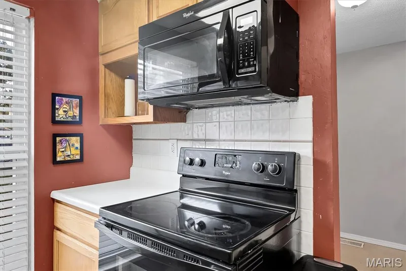 Kitchen area featuring a black electric range, a black over-the-range microwave, light wood cabinetry, a white countertop, and a white tiled backsplash — 43 Breezy Knoll Lane, Lake St. Louis, MO 63367