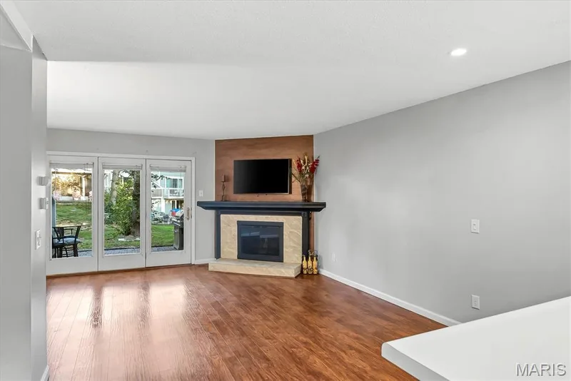 Living area featuring wood-finish flooring, a corner fireplace with a dark mantel and light-colored surround, and recessed lighting — 43 Breezy Knoll Lane, Lake St. Louis, MO 63367