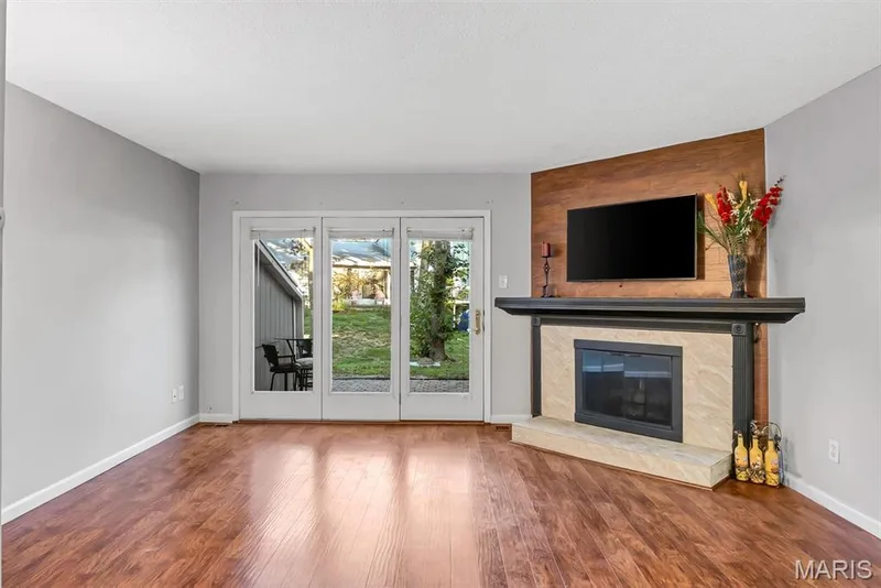Living area featuring wood-finish flooring, a fireplace with a stone surround and dark mantel, and a wood-paneled accent wall — 43 Breezy Knoll Lane, Lake St. Louis, MO 63367