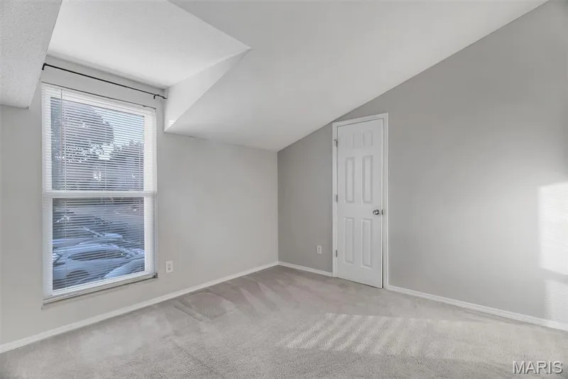 Room featuring light gray wall paint, matching gray carpet, a white multi-panel door, and a large window with white blinds — 43 Breezy Knoll Lane, Lake St. Louis, MO 63367