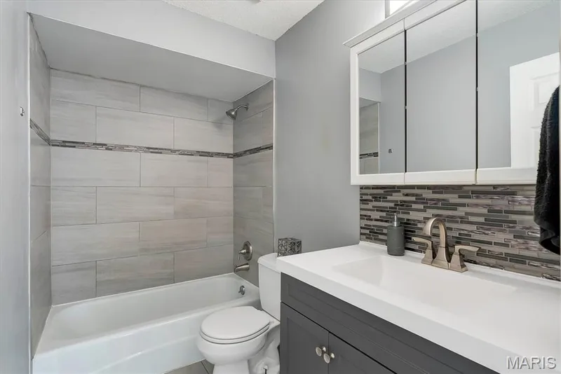 Bathroom featuring a combination shower and tub with large format tile surround and decorative accent band — 43 Breezy Knoll Lane, Lake St. Louis, MO 63367