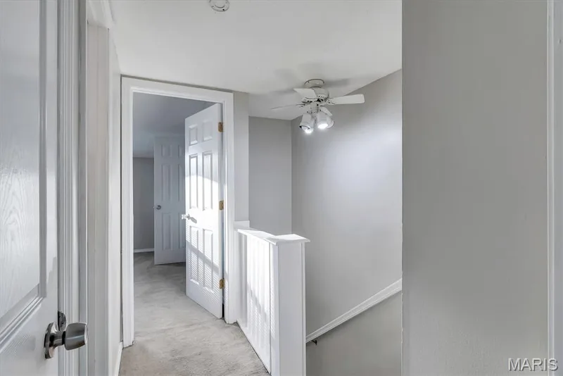 Hallway featuring gray carpeting, white balusters, and a ceiling fan with integrated lighting — 43 Breezy Knoll Lane, Lake St. Louis, MO 63367