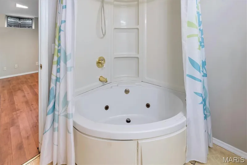 Corner jetted bathtub with integrated shower, brass fixtures, and a white surround — 43 Breezy Knoll Lane, Lake St. Louis, MO 63367