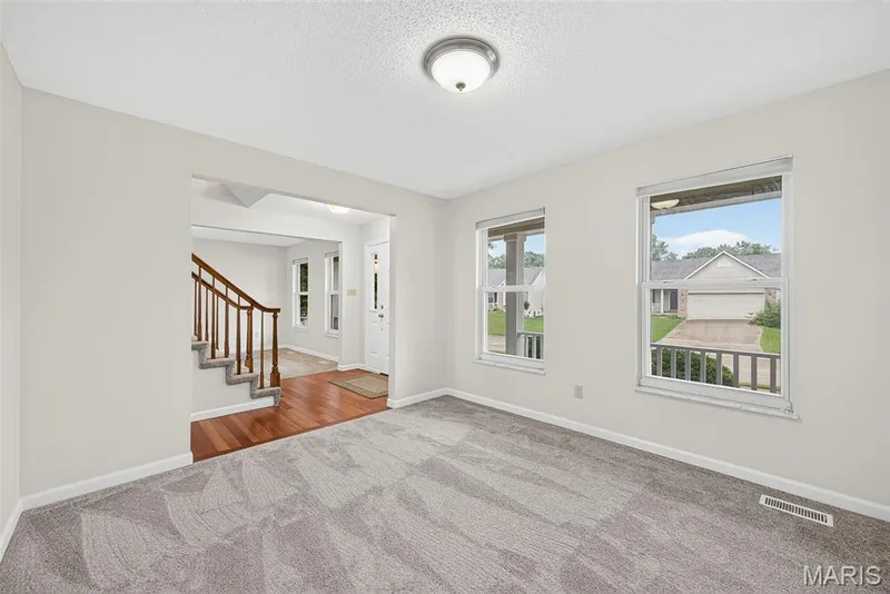 Carpeted room with a wide doorway opening to a wood-finish floor entry and staircase — 4014 Treeshadow Drive, St Peters, MO 63376