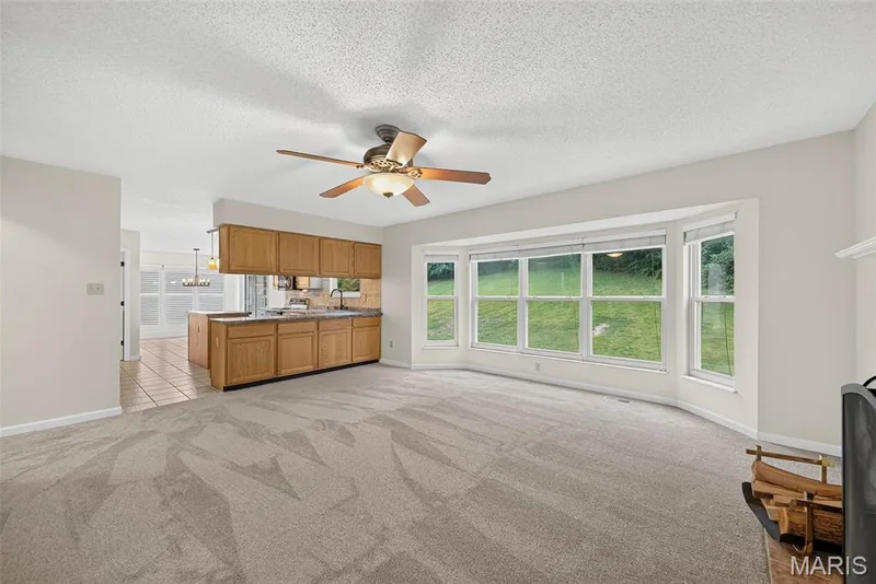 Expansive living area featuring a bay window, ceiling fan with light fixture, and plush carpeting — 4014 Treeshadow Drive, St Peters, MO 63376