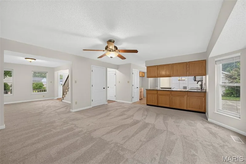 Spacious living area featuring neutral carpeting, a ceiling fan with integrated lighting, and multiple windows for natural light — 4014 Treeshadow Drive, St Peters, MO 63376
