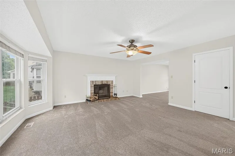 Spacious living area featuring a brick fireplace with a white mantel, bay windows, and neutral carpet — 4014 Treeshadow Drive, St Peters, MO 63376