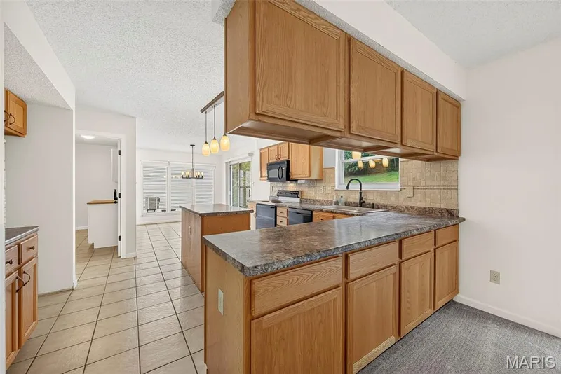 Kitchen featuring wood cabinetry, dark countertops, tile backsplash, and a central island — 4014 Treeshadow Drive, St Peters, MO 63376