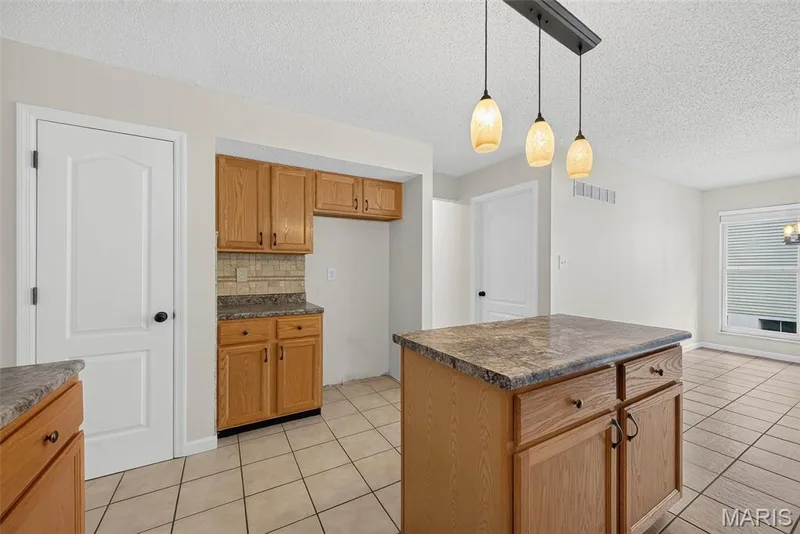 Kitchen area featuring a central island with a stone-finish countertop, wood cabinetry, and a three-light pendant fixture — 4014 Treeshadow Drive, St Peters, MO 63376
