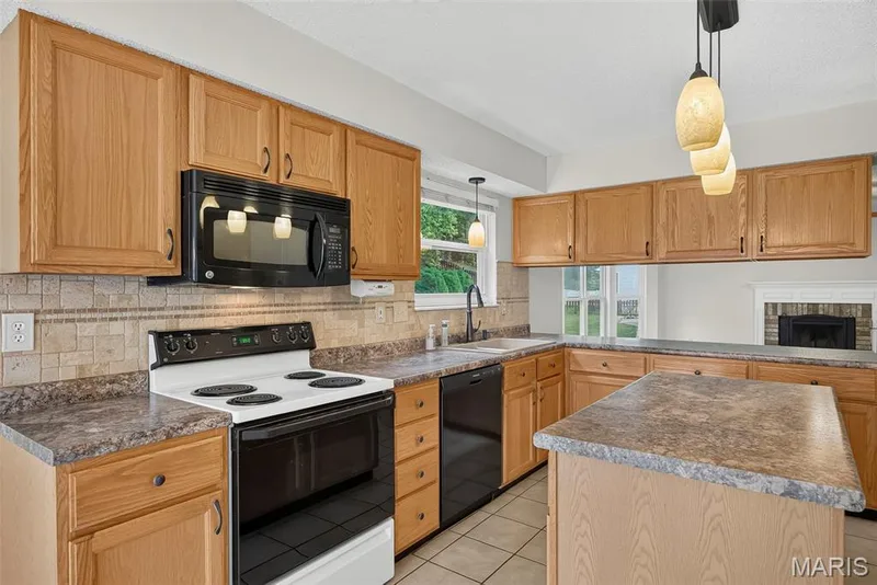 Kitchen featuring wood-finish cabinetry, black appliances, a tile backsplash, and a central island with a contrasting countertop — 4014 Treeshadow Drive, St Peters, MO 63376