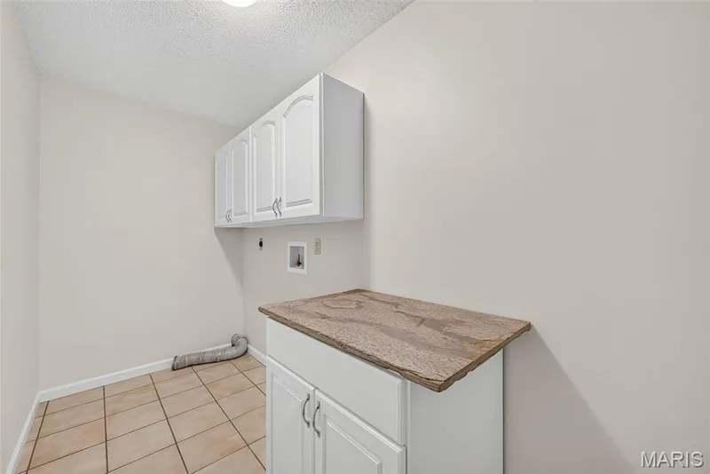 Laundry room featuring white cabinetry, a stone-finish countertop, and tile flooring — 4014 Treeshadow Drive, St Peters, MO 63376