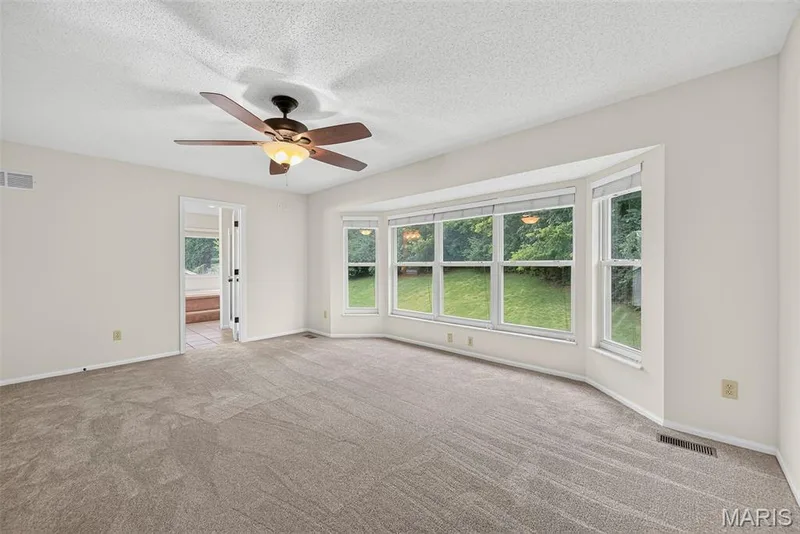 Spacious room featuring a bay window, neutral carpeting, light-toned walls, a ceiling fan with integrated lighting, and a doorway with double doors — 4014 Treeshadow Drive, St Peters, MO 63376