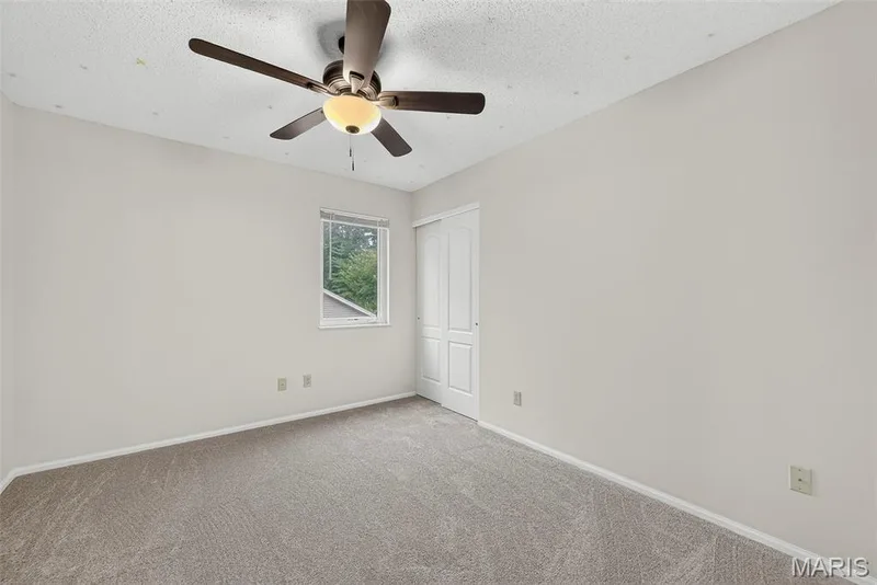 Carpeted room featuring a ceiling fan with light fixture, a window, and a white bi-fold closet door — 4014 Treeshadow Drive, St Peters, MO 63376