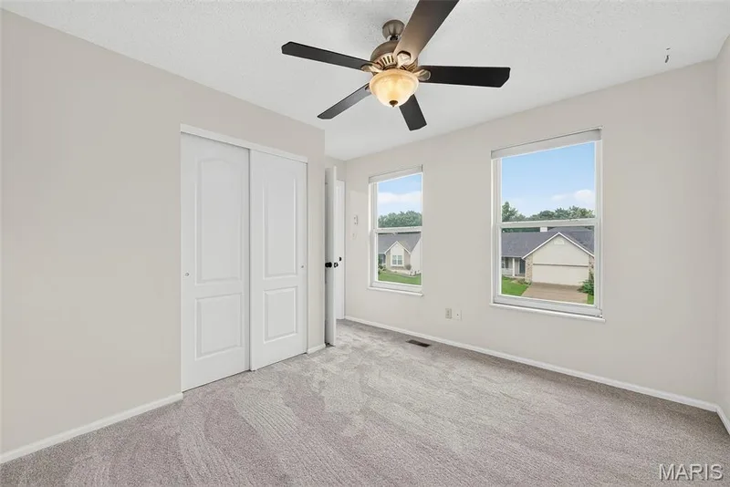 Carpeted interior space featuring two windows, a ceiling fan with integrated lighting, and a closet with bifold doors — 4014 Treeshadow Drive, St Peters, MO 63376