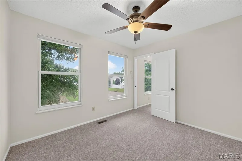 Bright room featuring two large windows, a ceiling fan with integrated lighting, neutral wall paint, and gray carpet flooring — 4014 Treeshadow Drive, St Peters, MO 63376