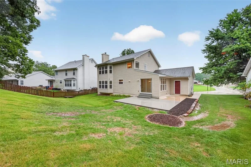 Expansive backyard featuring a manicured lawn, a large concrete patio, and a dedicated garden bed — 4014 Treeshadow Drive, St Peters, MO 63376