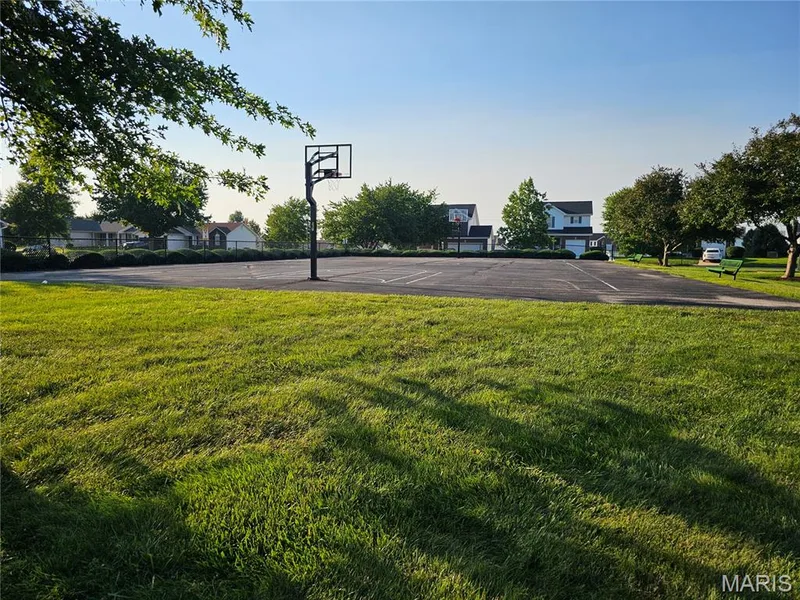 Expansive green space featuring a paved court with a basketball hoop, surrounded by mature trees and residential structures in the background — 618 Homerun Drive, O'Fallon, MO 63366
