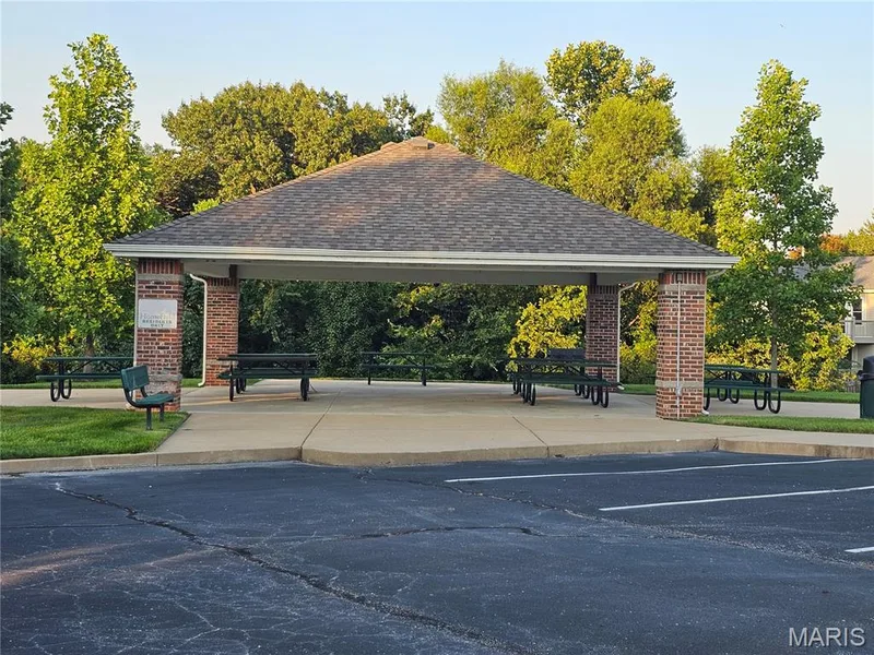 Community pavilion featuring a shingled roof, brick columns, concrete flooring, and mature surrounding trees — 618 Homerun Drive, O'Fallon, MO 63366