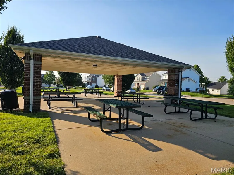 Community pavilion featuring a shingled roof, brick columns, concrete flooring, and multiple picnic tables — 618 Homerun Drive, O'Fallon, MO 63366