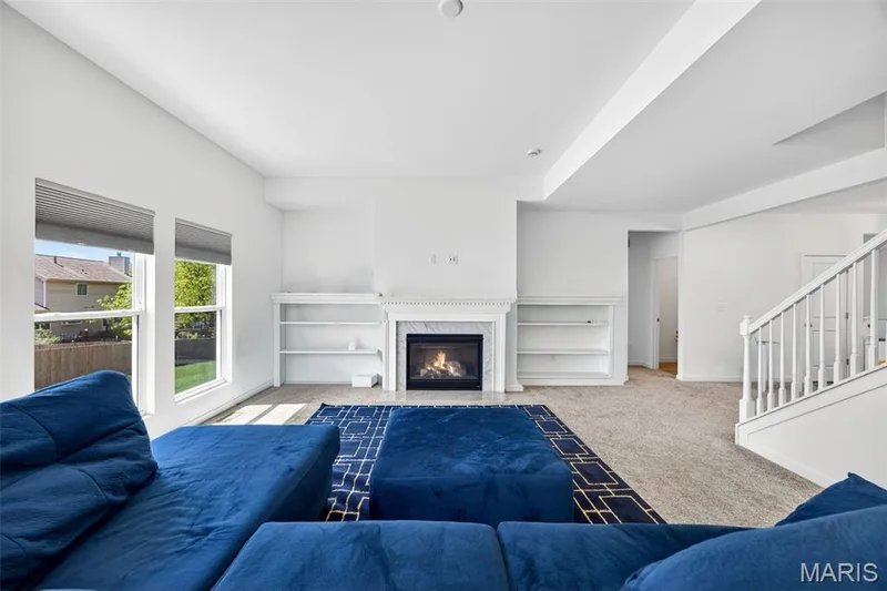Living area featuring a fireplace with a marble-look surround, integrated shelving, large windows with exterior views, and a carpeted floor — 365 Kreder Ridge Circle, St Charles, MO 63304