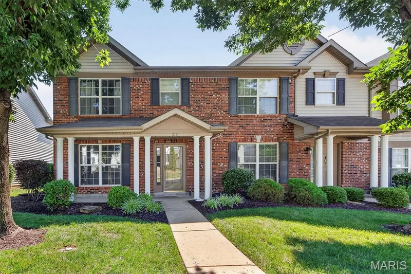Brick and siding exterior featuring a covered porch entry with white columns, dark shutters, and a concrete walkway — 916 Carpathian Drive, Lake St. Louis, MO 63367