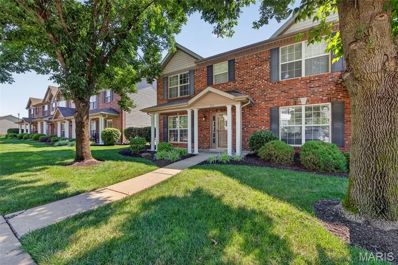 Red brick facade with contrasting dark shutters, a covered porch entrance, and mature tree landscaping — 916 Carpathian Drive, Lake St. Louis, MO 63367
