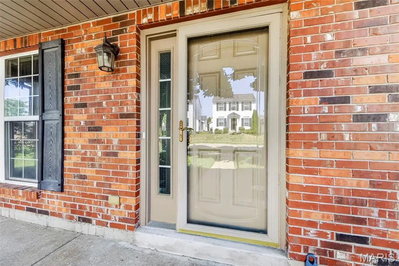 Brick exterior featuring a paneled entry door with glass inserts, a storm door, and a built-in exterior light fixture — 916 Carpathian Drive, Lake St. Louis, MO 63367
