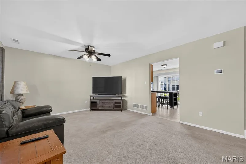 Spacious living area featuring neutral-toned carpeting, light-colored walls, and a ceiling fan with integrated lighting — 916 Carpathian Drive, Lake St. Louis, MO 63367