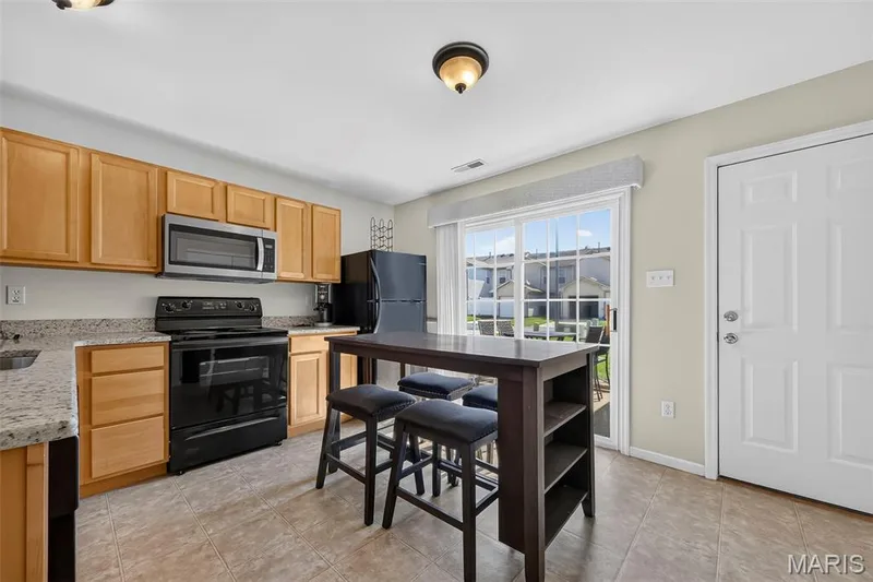 Kitchen featuring light wood cabinetry, granite-style countertops, stainless steel microwave, black electric range, and a glass sliding door — 916 Carpathian Drive, Lake St. Louis, MO 63367