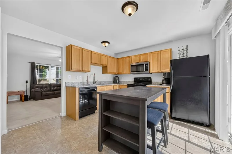 Kitchen featuring wood cabinetry, granite-finish countertops, and black appliances — 916 Carpathian Drive, Lake St. Louis, MO 63367
