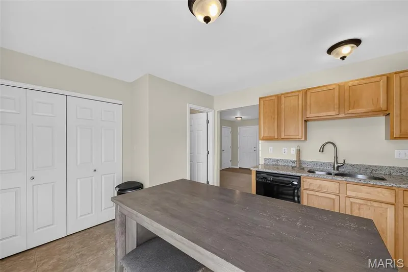 Kitchen featuring a wood-finish island, light wood cabinetry, granite countertops, and a stainless steel sink with a gooseneck faucet — 916 Carpathian Drive, Lake St. Louis, MO 63367