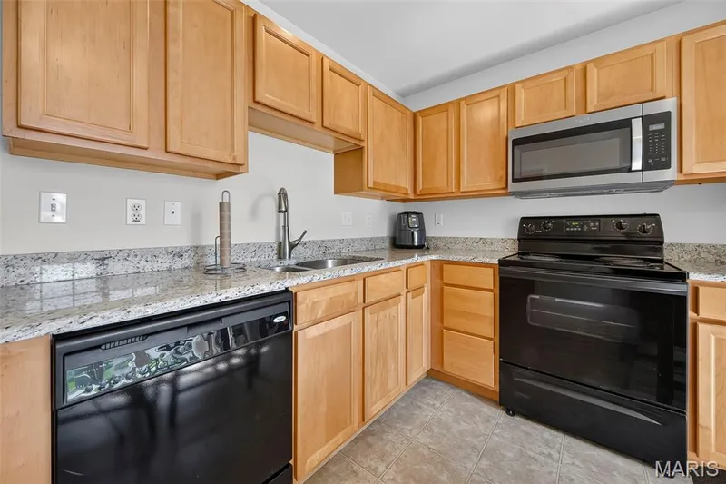 Kitchen featuring light wood cabinetry, stone countertops, stainless steel microwave, black electric range, and black dishwasher — 916 Carpathian Drive, Lake St. Louis, MO 63367