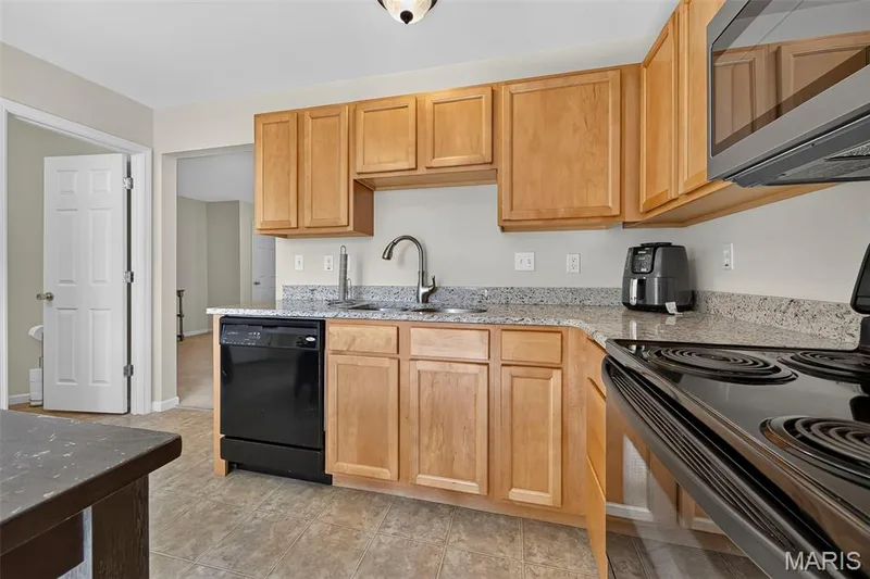 Well-appointed kitchen featuring light wood cabinetry, speckled countertops, a double basin sink with a high-arc faucet, and a black electric range with an overhead microwave — 916 Carpathian Drive, Lake St. Louis, MO 63367