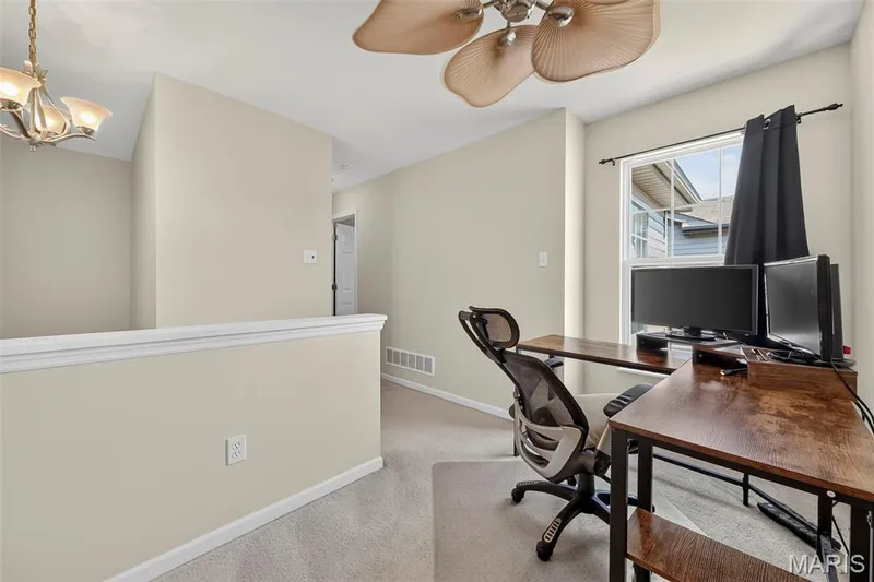 Carpeted landing area featuring a ceiling fan with light fixture, a window with black drapes, and a partial wall with white trim — 916 Carpathian Drive, Lake St. Louis, MO 63367