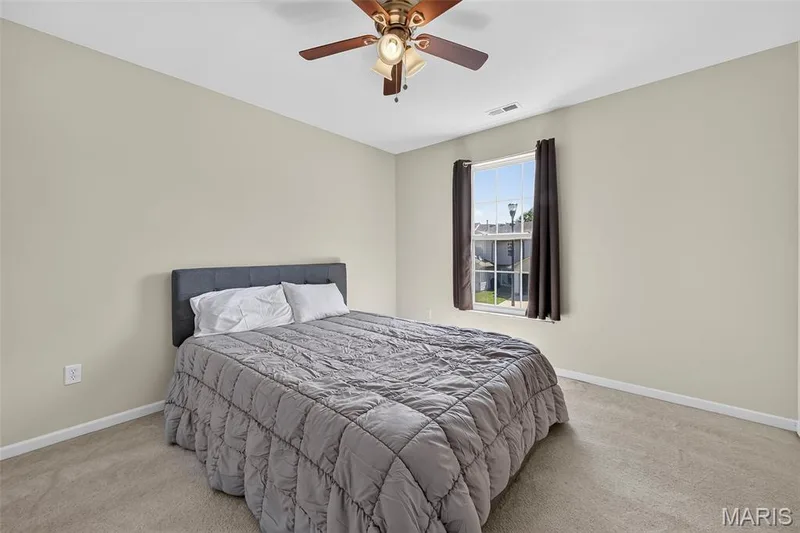 Carpeted bedroom featuring a ceiling fan with integrated lighting, a window with dark drapery, and neutral wall tones — 916 Carpathian Drive, Lake St. Louis, MO 63367