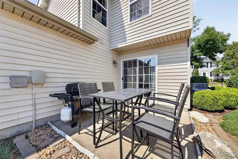 Concrete patio area featuring light-toned siding, sliding glass door access, and exterior wall lighting — 916 Carpathian Drive, Lake St. Louis, MO 63367