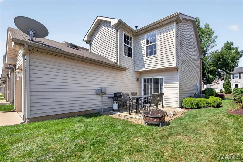 Rear exterior featuring light-toned horizontal siding, a concrete patio, and a sliding glass door — 916 Carpathian Drive, Lake St. Louis, MO 63367