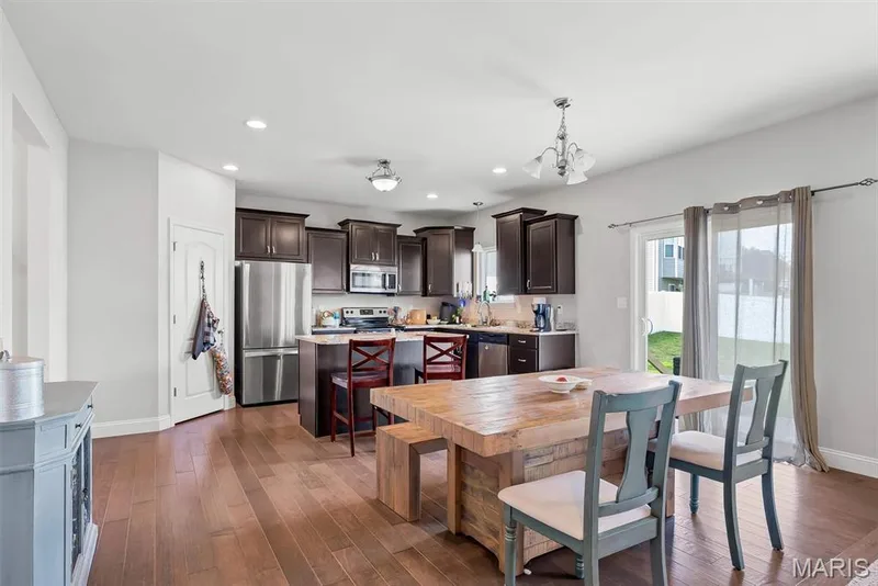 Open-concept kitchen and dining area featuring rich wood-finish flooring, dark cabinetry, and stainless steel appliances — 225 Thorn Brook Drive, O'Fallon, MO 63366