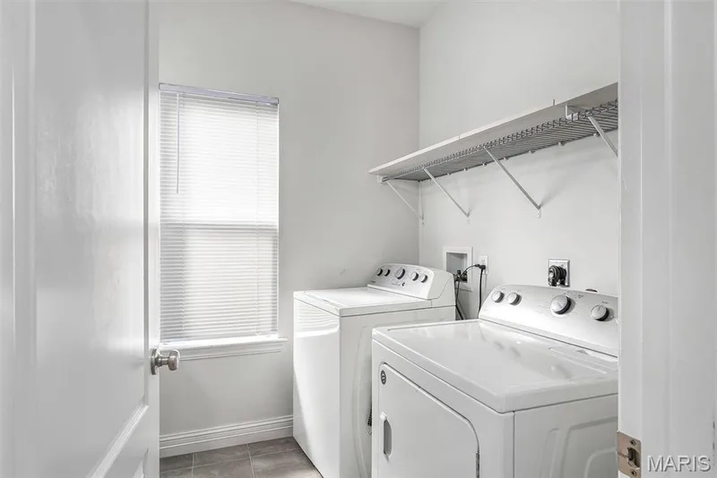 Dedicated laundry room featuring a window with blinds, tile flooring, and a wall-mounted storage shelf — 225 Thorn Brook Drive, O'Fallon, MO 63366