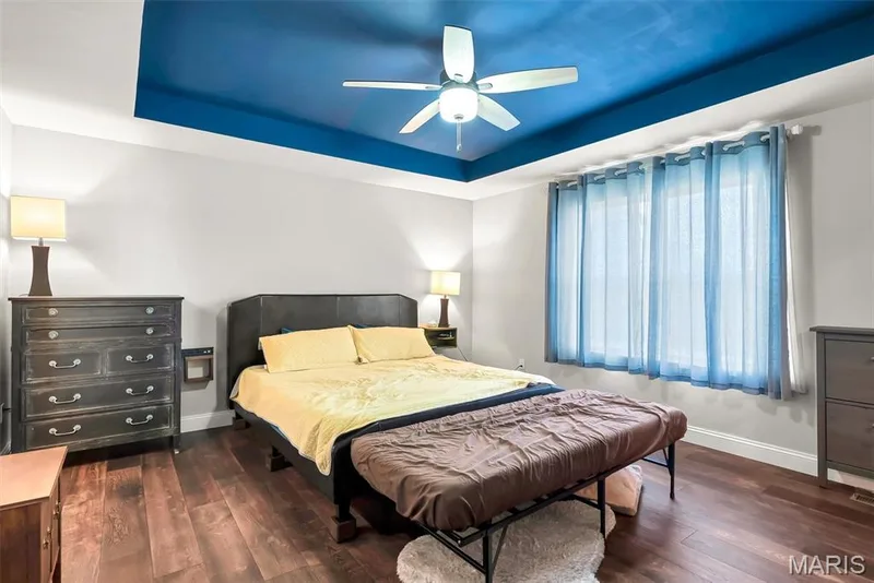 Tray ceiling with a blue accent, wood-finish flooring, ceiling fan, and large window with blinds — 225 Thorn Brook Drive, O'Fallon, MO 63366