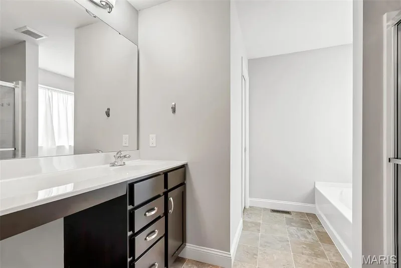 Spa-inspired primary bathroom featuring a lengthy white quartz countertop, dark wood-finish vanity with multiple storage drawers, chrome faucet fixtures, and a large framed mirror — 225 Thorn Brook Drive, O'Fallon, MO 63366