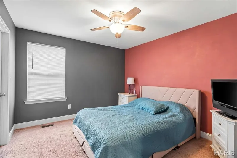 Spacious bedroom featuring a neutral upholstered bed frame, wood-finish flooring, and soft area rug — 225 Thorn Brook Drive, O'Fallon, MO 63366