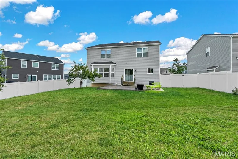 Expansive backyard featuring a manicured lawn with white vinyl fencing, mature landscaping, and multiple residential structures visible — 225 Thorn Brook Drive, O'Fallon, MO 63366