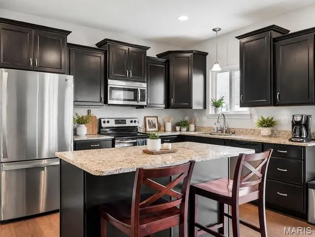 Kitchen featuring dark wood cabinetry, granite countertops, stainless steel appliances, a center island, and wood-finish flooring — 225 Thorn Brook Drive, O'Fallon, MO 63366