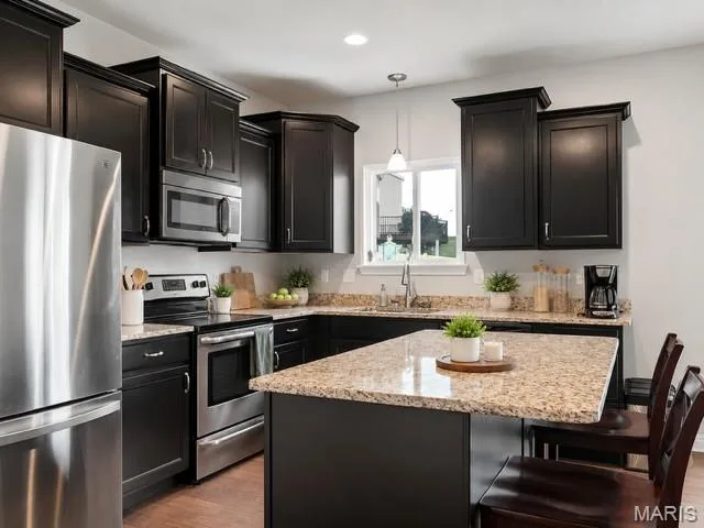 Kitchen featuring dark cabinetry, stainless steel appliances, speckled stone countertops, and a center island with bar seating — 225 Thorn Brook Drive, O'Fallon, MO 63366