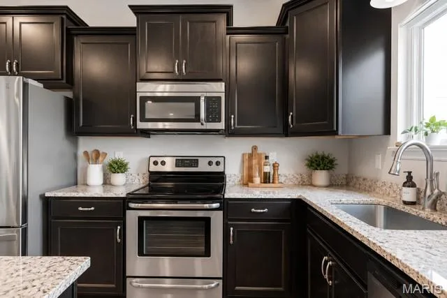 Dark wood cabinetry with crown molding, stainless steel appliances, speckled stone countertops, and a stainless steel sink with a gooseneck faucet — 225 Thorn Brook Drive, O'Fallon, MO 63366