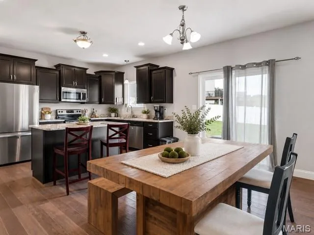 Open-concept kitchen with dark wood cabinetry, stainless steel appliances, a kitchen island with seating, and wood-finish flooring — 225 Thorn Brook Drive, O'Fallon, MO 63366