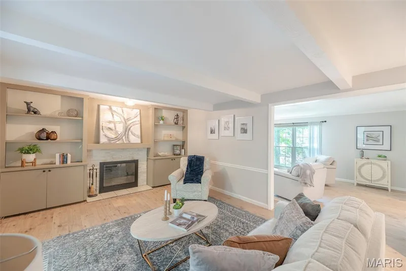 Bright, open-concept living area featuring wood-finish flooring, built-in cabinetry with display shelving, and a gas fireplace with surround millwork — 1526 Candish Lane, Chesterfield, MO 63017