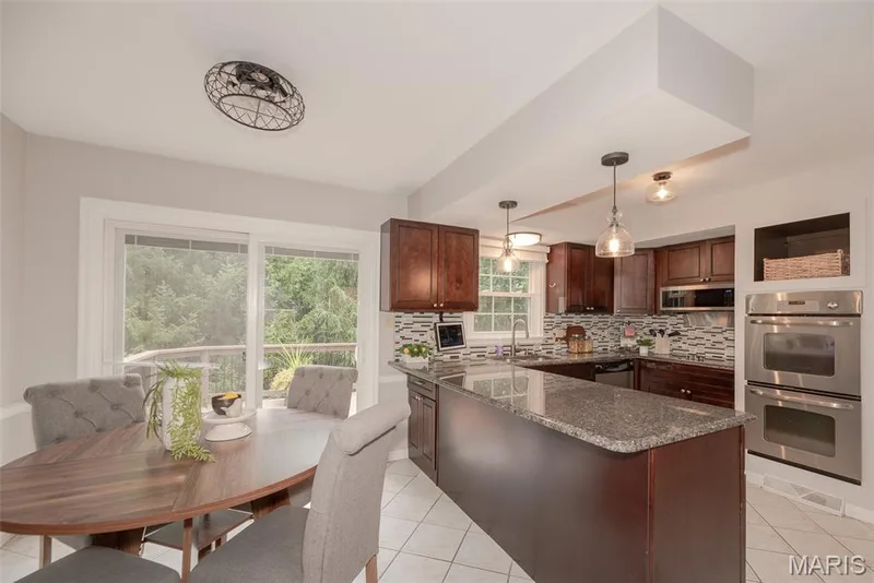 Kitchen featuring dark wood-finish cabinetry, a central island with a stone-finish countertop, dual built-in stainless steel ovens, and a tile backsplash — 1526 Candish Lane, Chesterfield, MO 63017